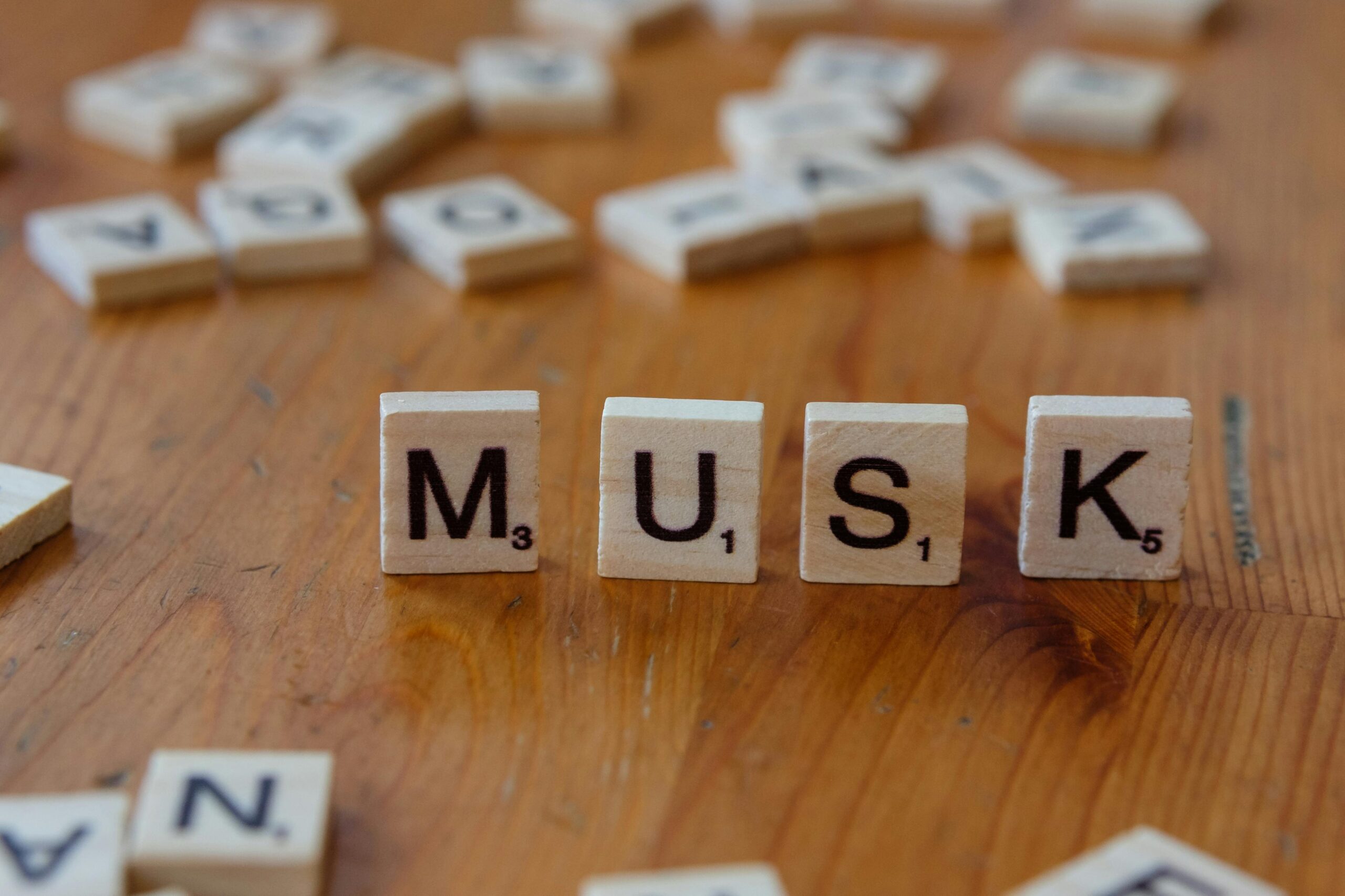 Close-up of Scrabble tiles spelling 'MUSK' on a wooden table, ideal for business and innovation themes.